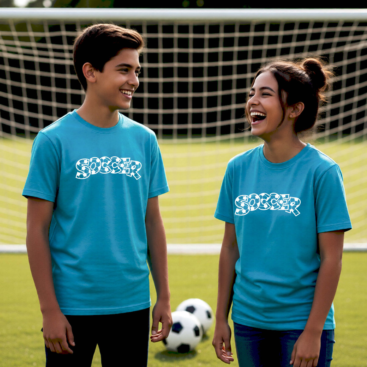 Two young athletics wearing matching bright blue t-shirt, standing on a soccer field in front of a goal net. with a white graphic of the word 'SOCCER' in a stylish soccer pattern printed on the chests.