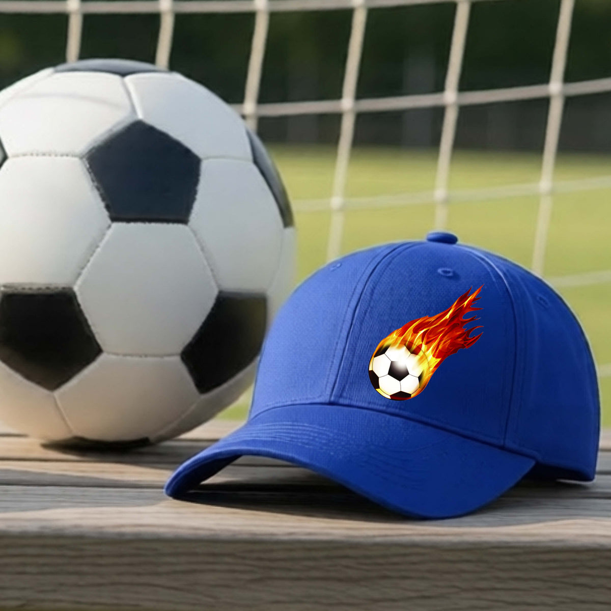 A close-up of a royal blue hat sitting on an outdoor bench next to a soccer ball with a white graphic of a soccer ball shooting through air and trailing yellow, red and orange flames behind it, printed on the front.