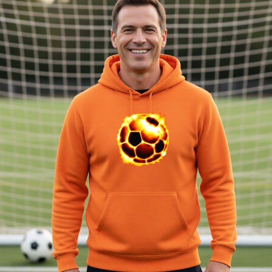 A smiling man wearing an orange hoodie with a glowing soccer ball graphic on the chest, standing on a soccer field in front of a goal net.