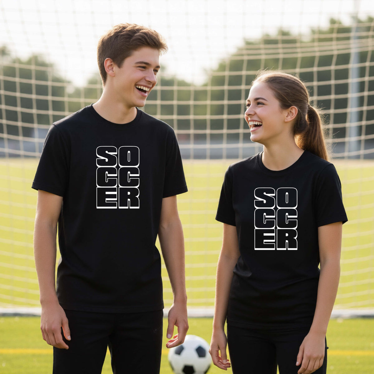 Two young athletes wearing matching black t-shirts, standing in front of a soccr goal and balls, with a white graphic of the word ‘SOCCER’ stacked in a 2x3 arrangement, printed on the chest.