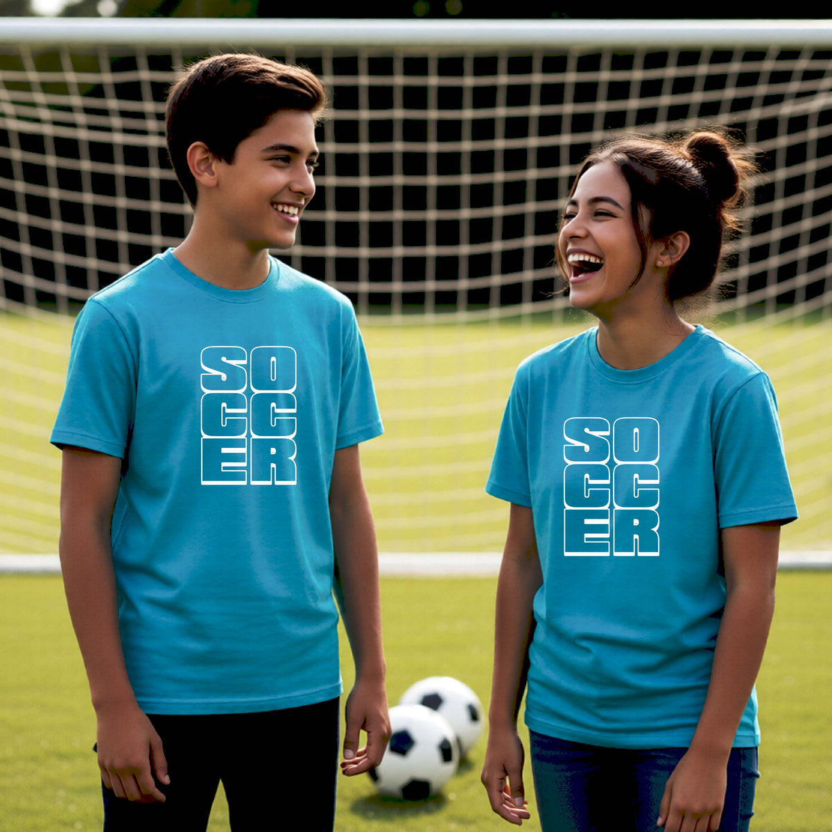 Two young athletes wearing matching bright blue t-shirts, standing in front of a soccr goal and balls, with a white graphic of the word ‘SOCCER’ stacked in a 2x3 arrangement, printed on the chest.