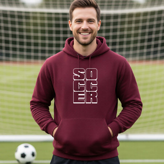 A smiling man wearing a maroon hoodie pullover standing on a soccer field in front of a goal net. with a white graphic of the word ‘SOCCER’ stacked in a 2x3 arrangement, printed on the chest.