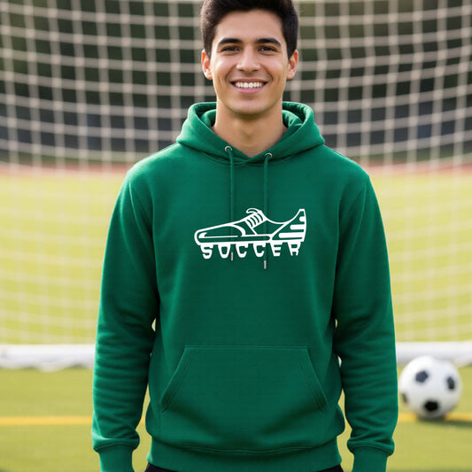 A smiling man, standing on a soccer field in front of a goal net. wearing a green hoodie pullover with a white soccer cleat graphic and the word 'SOCCER' printed on the chest.