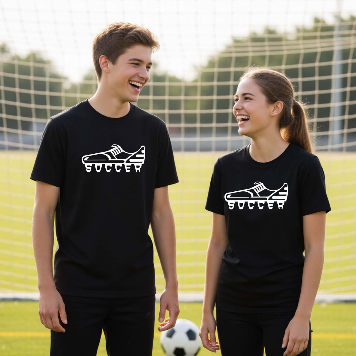 A young man and woman standing on a soccer field wearing matching black t-shirts with a white soccer cleat graphic and the word 'SOCCER' printed on the chest.