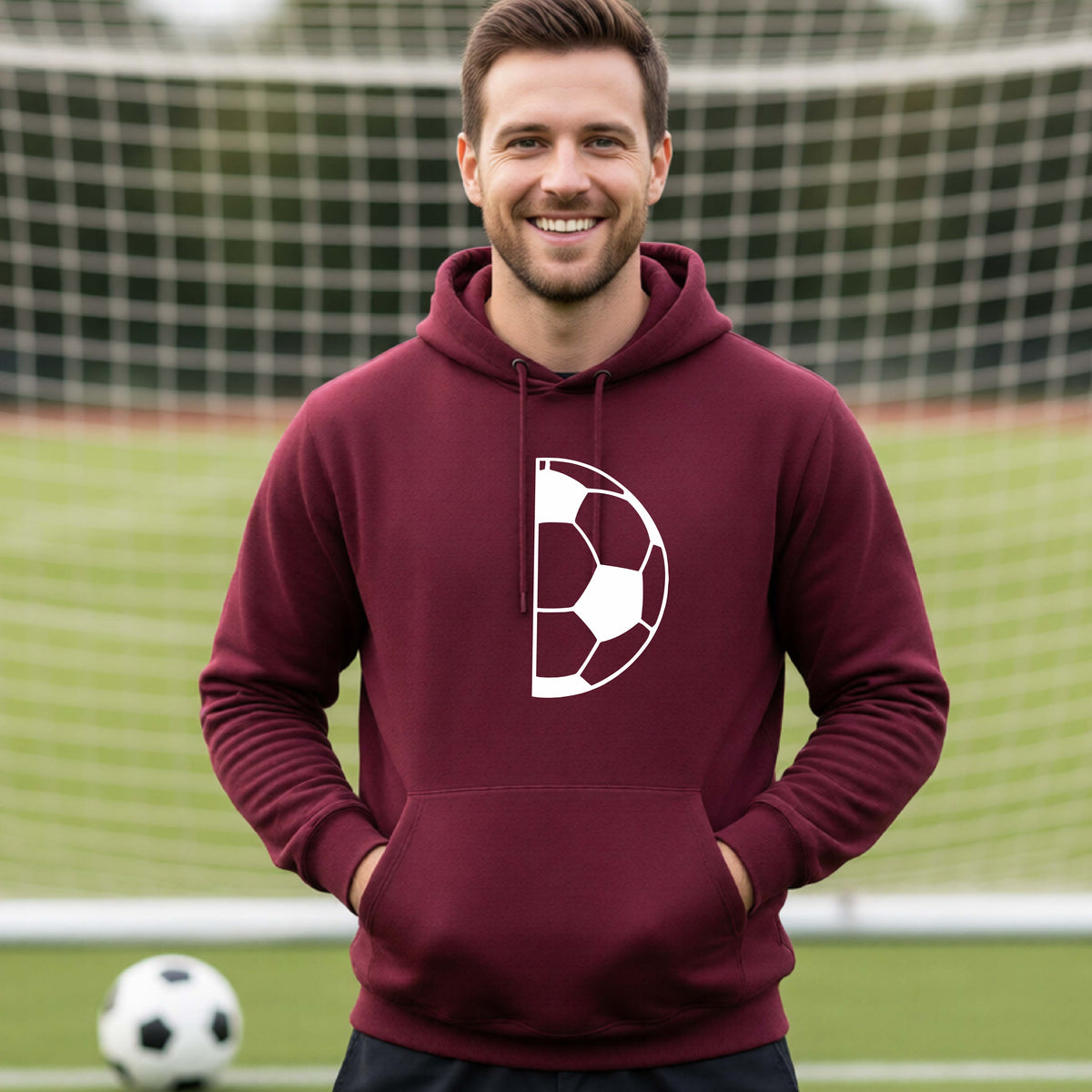 A man laughing on a soccer field wearing a maroon hoodie pullover with a white half soccer ball graphic inside a semicircle on the chest.