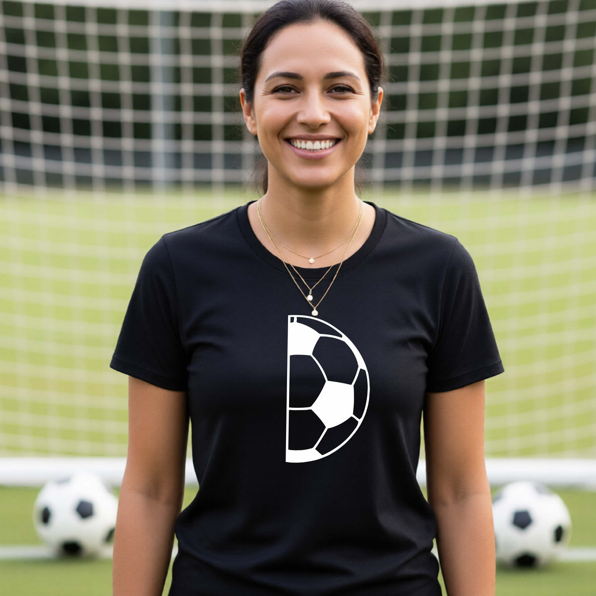 A woman laughing on a soccer field wearing a black t-shirt with a white half soccer ball graphic inside a semicircle on the chest.