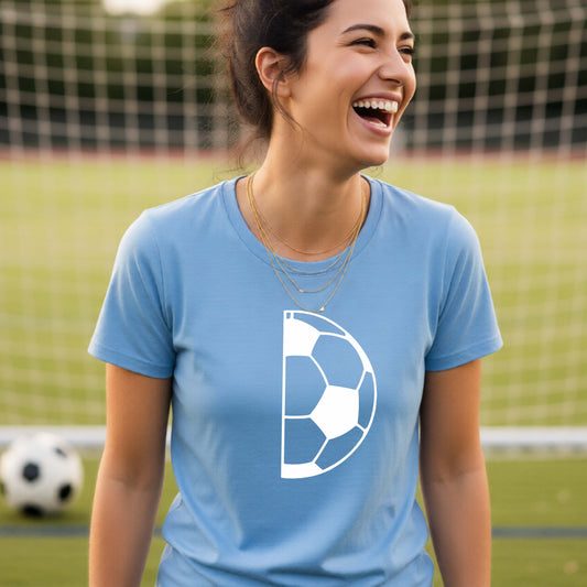 A woman laughing on a soccer field wearing a light blue t-shirt with a white half soccer ball graphic inside a semicircle on the chest.