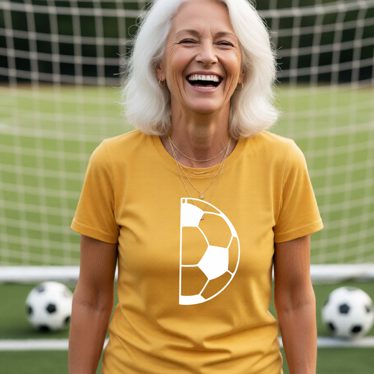 A woman laughing on a soccer field wearing a gold t-shirt with a white half soccer ball graphic inside a semicircle on the chest.