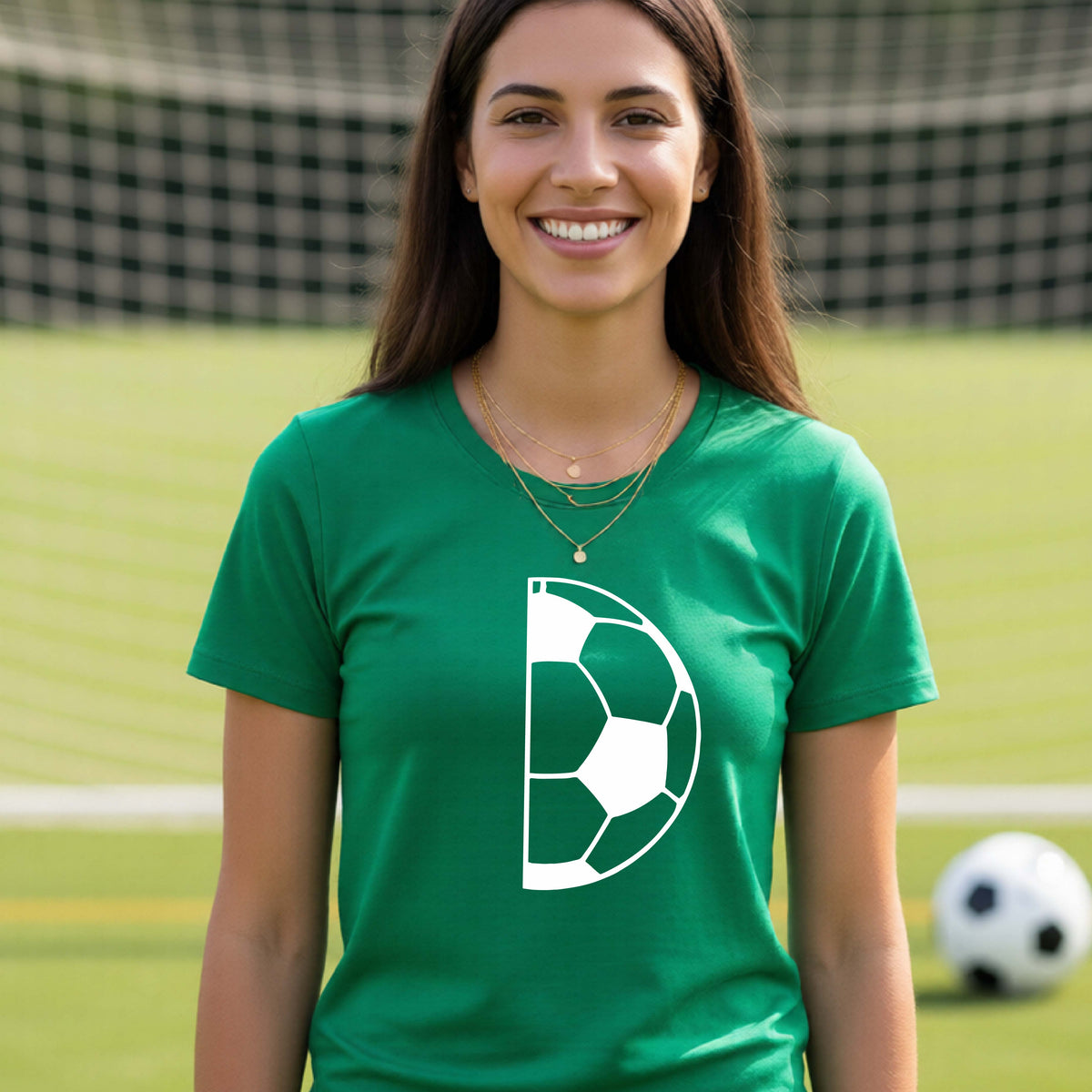A woman laughing on a soccer field wearing a green t-shirt with a white half soccer ball graphic inside a semicircle on the chest.