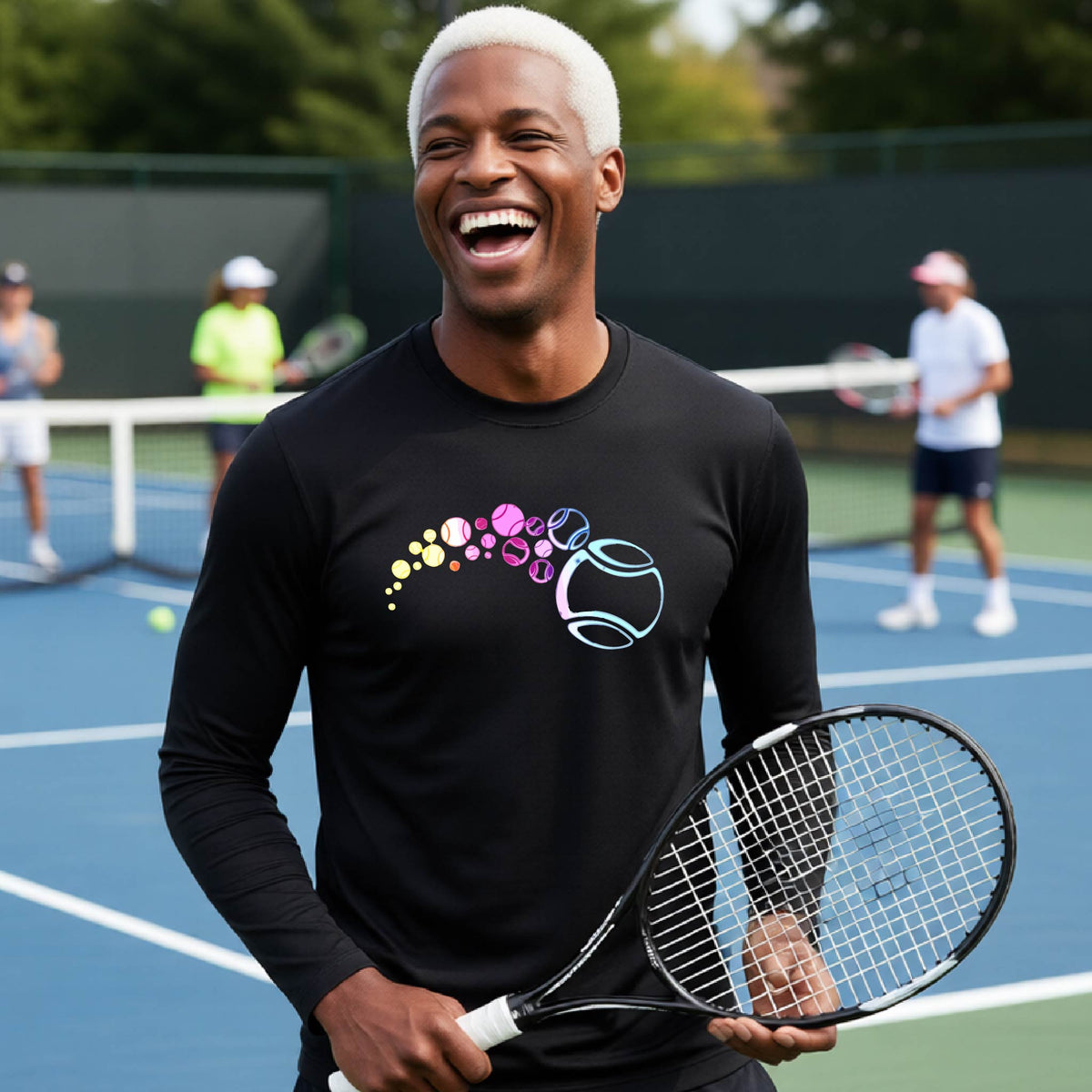 A man on a tennis court wearing a black long-sleeve t-shirt with a graphic of pastel gradient colored tennis balls arcing in flight and gradually getting larger.