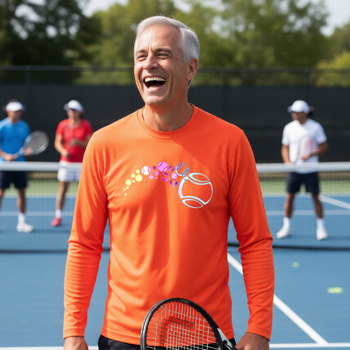 A man on a tennis court wearing an orange long-sleeve t-shirt with a graphic of pastel gradient colored tennis balls arcing in flight and gradually getting larger.