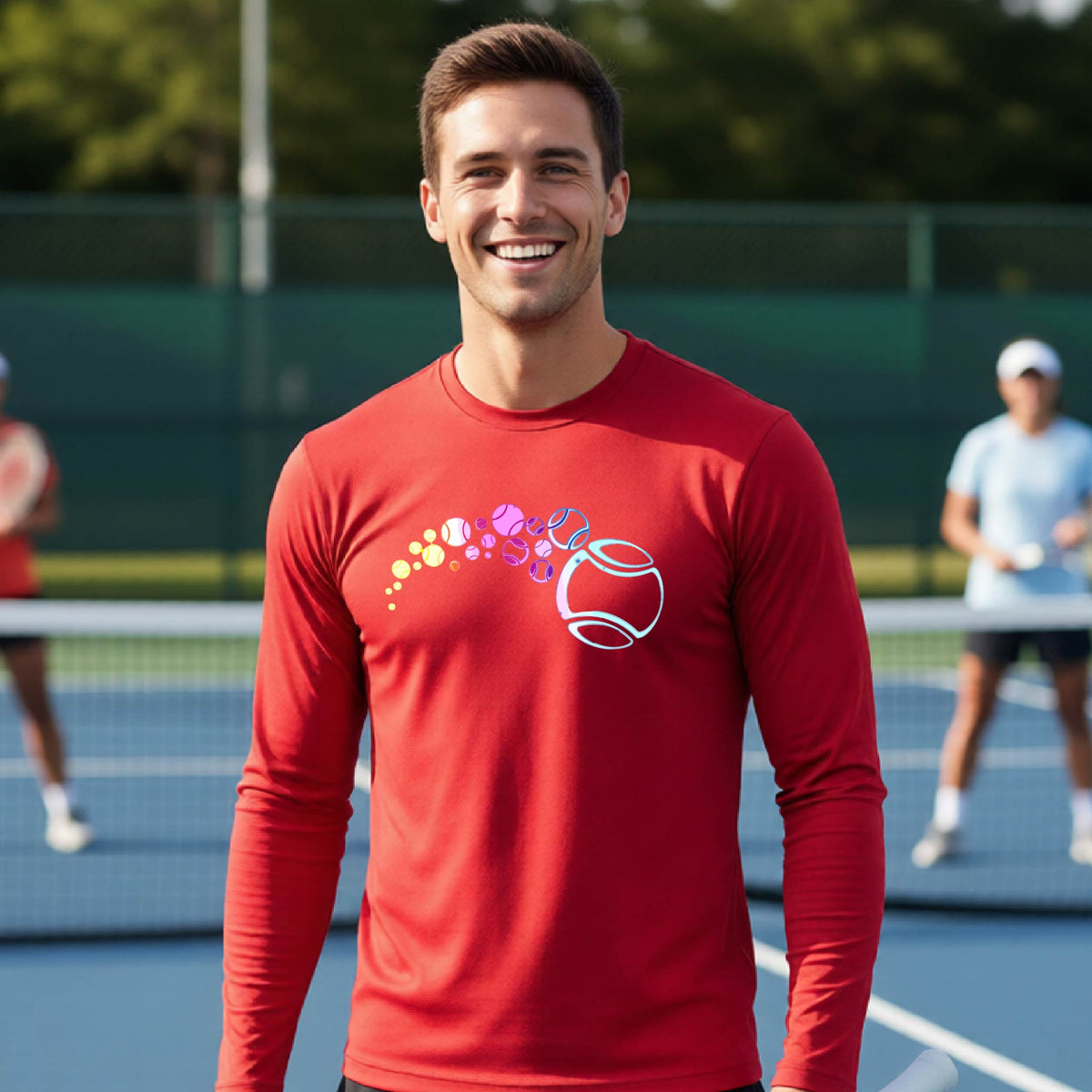 A man on a tennis court wearing a red long-sleeve t-shirt with a graphic of pastel gradient colored tennis balls arcing in flight and gradually getting larger.