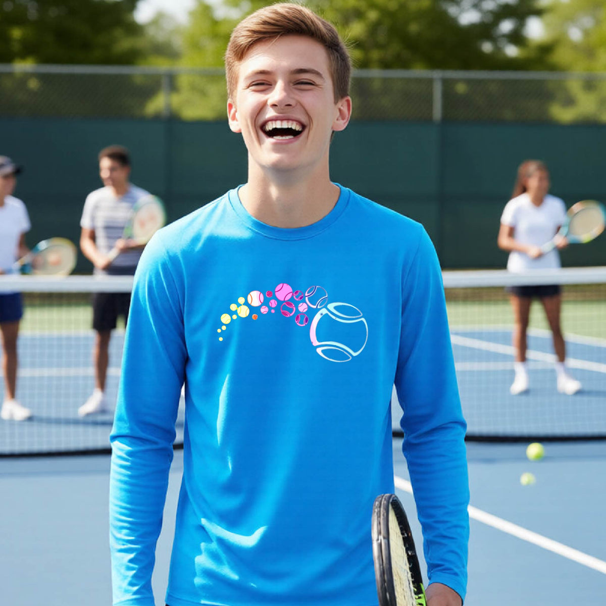 A young person on a tennis court wearing a bright blue long-sleeve t-shirt with a graphic of pastel gradient colored tennis balls arcing in flight and gradually getting larger.