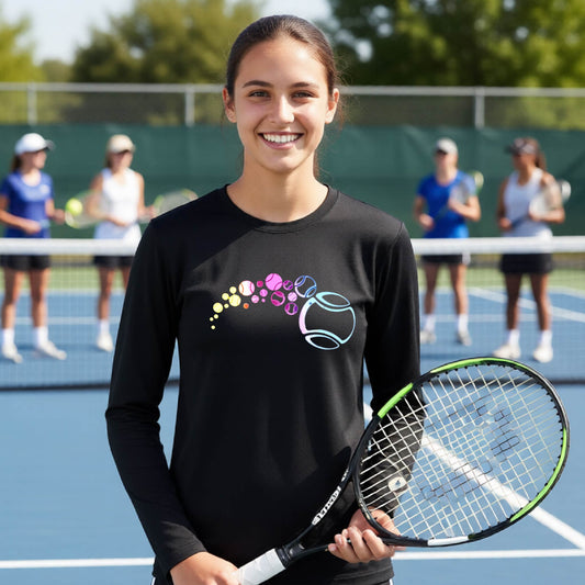 A young person on a tennis court wearing a black long-sleeve t-shirt with a graphic of pastel gradient colored tennis balls arcing in flight and gradually getting larger.