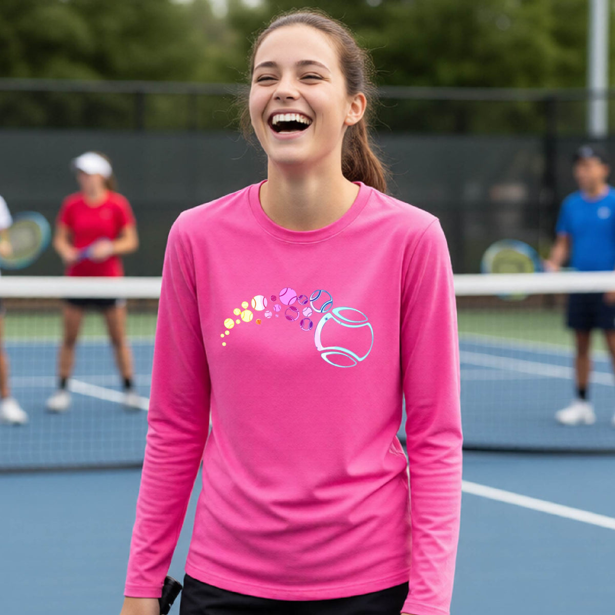A young person on a tennis court wearing a pink long-sleeve t-shirt with a graphic of pastel gradient colored tennis balls arcing in flight and gradually getting larger.