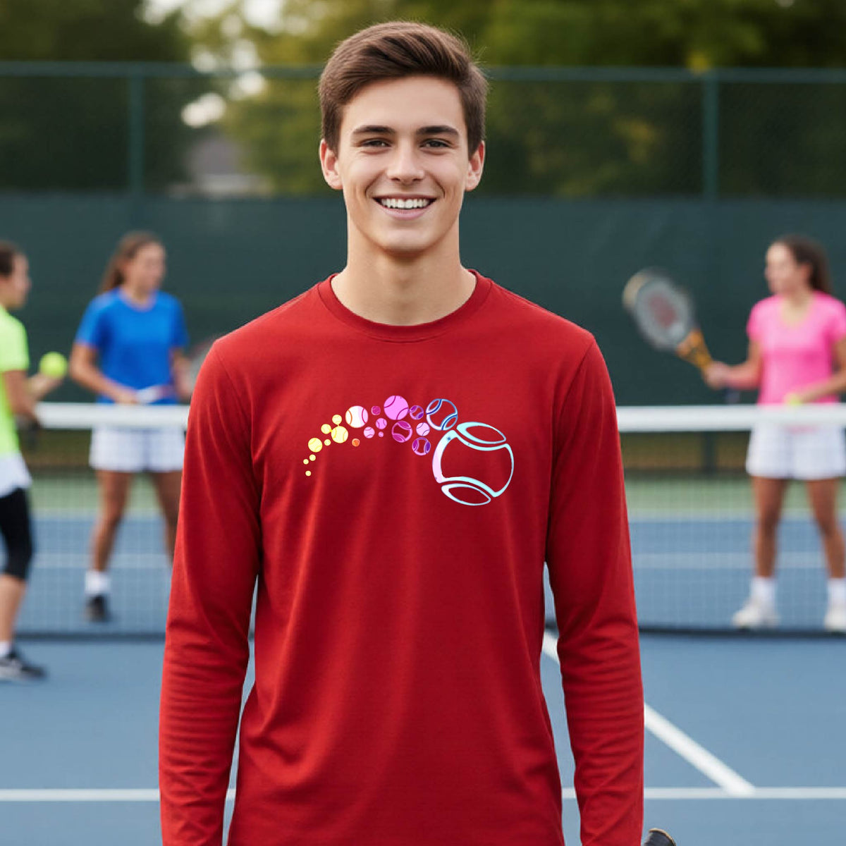 A young person on a tennis court wearing a red long-sleeve t-shirt with a graphic of pastel gradient colored tennis balls arcing in flight and gradually getting larger.