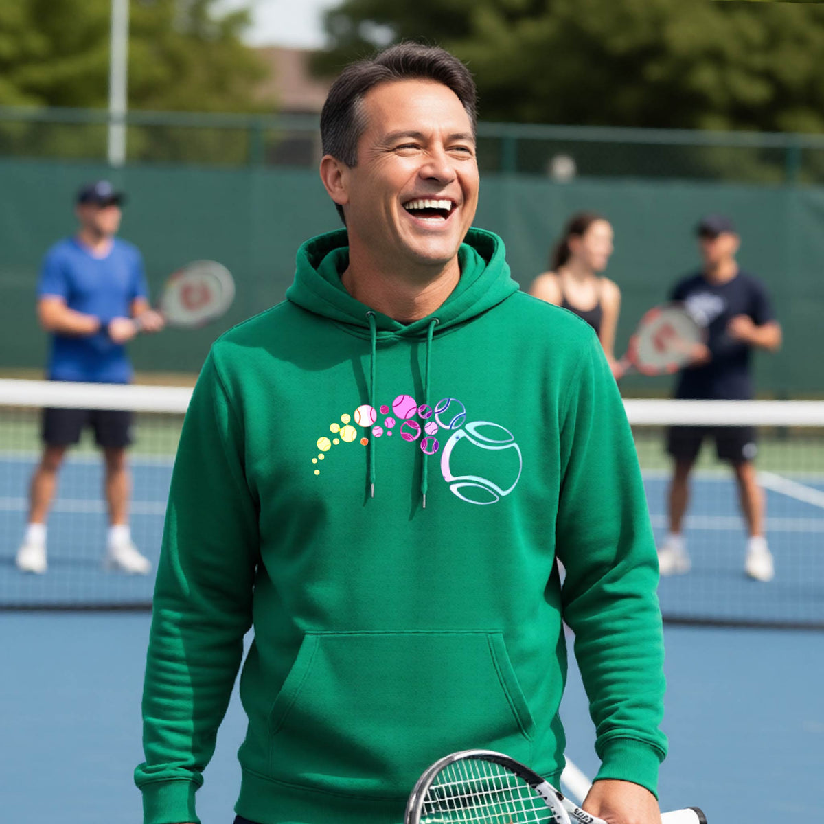 A man on a tennis court wearing a green hoodie pullover with a graphic of pastel gradient colored tennis balls arcing in flight and gradually getting larger.