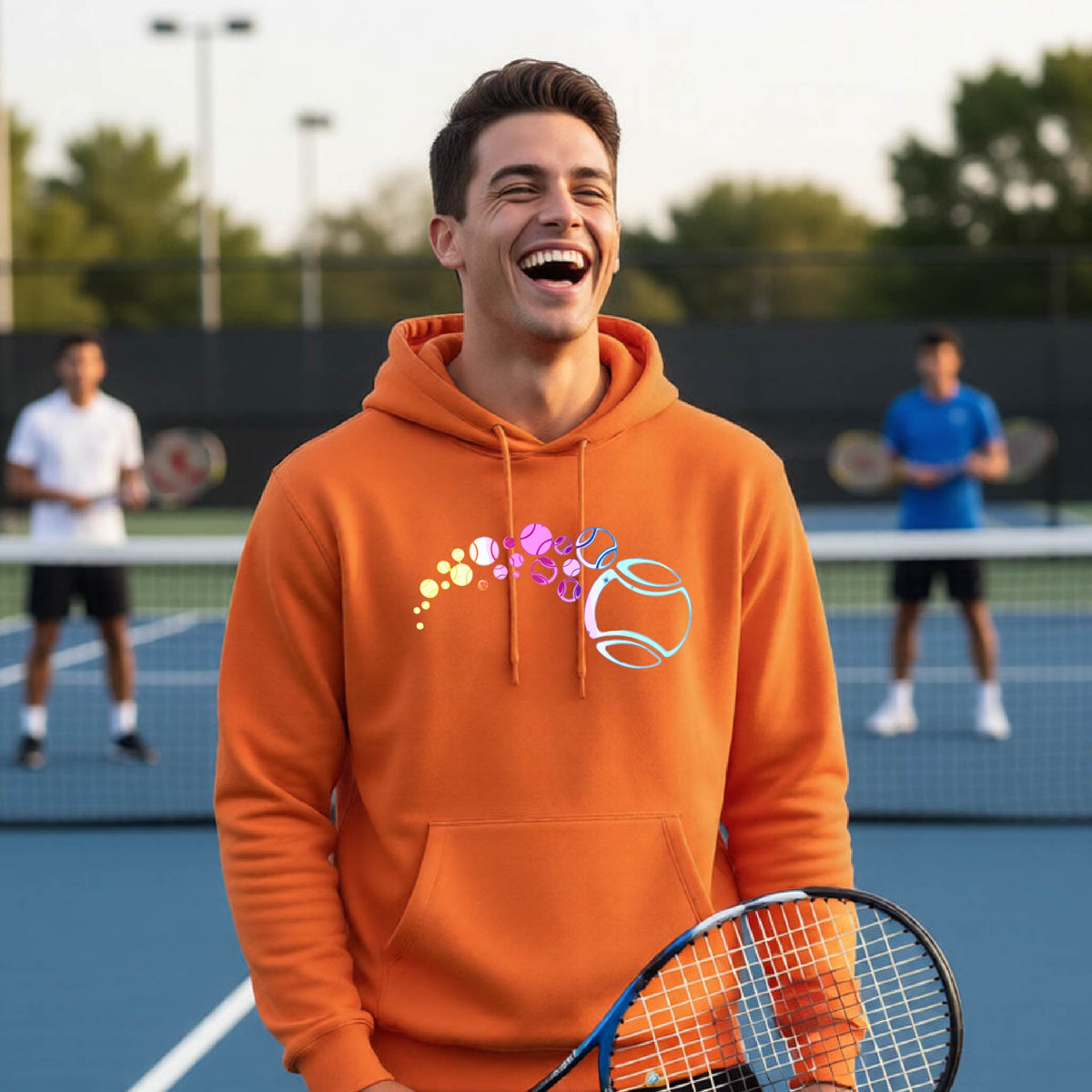A man on a tennis court wearing an orange hoodie pullover with a graphic of pastel gradient colored tennis balls arcing in flight and gradually getting larger.