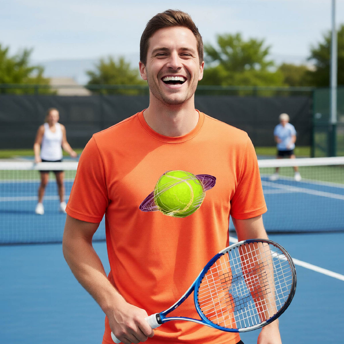 A man on a tennis court wearing an orange short-sleeve t-shirt with a graphic of a tennis ball in orbit, holding a tennis racket. Other players are visible in the background on the court.