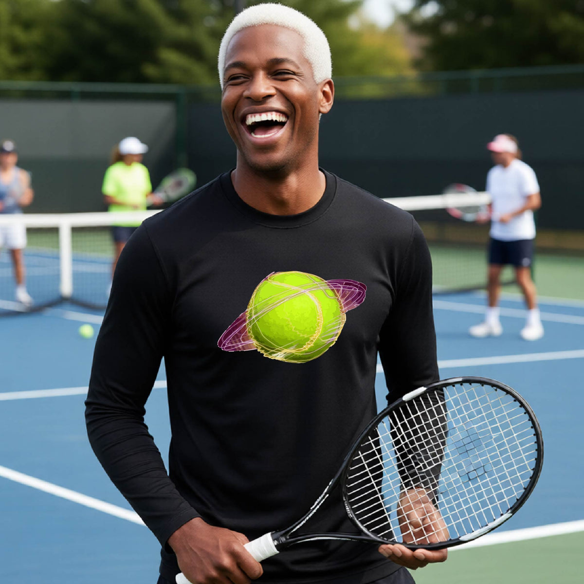 A man on a tennis court wearing a black long-sleeve t-shirt with a graphic of a tennis ball in orbit, holding a tennis racket. Other players are visible in the background on the court.