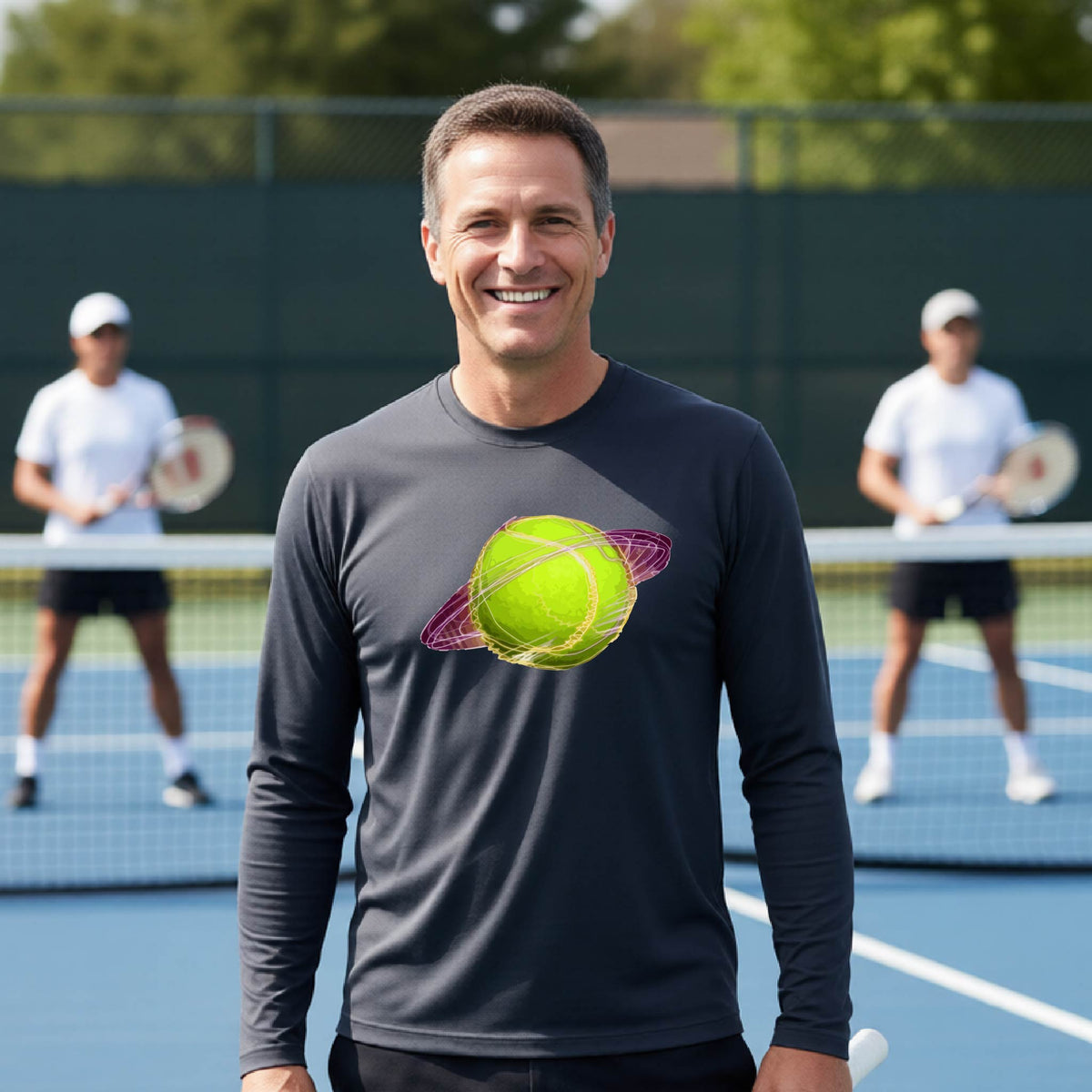 A man on a tennis court wearing a dark gray long-sleeve t-shirt with a graphic of a tennis ball in orbit, holding a tennis racket. Other players are visible in the background on the court.