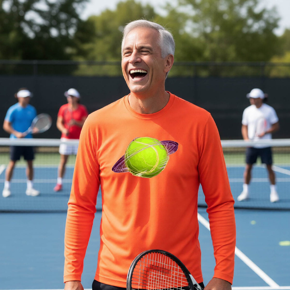 A man on a tennis court wearing an orange long-sleeve t-shirt with a graphic of a tennis ball in orbit, holding a tennis racket. Other players are visible in the background on the court.