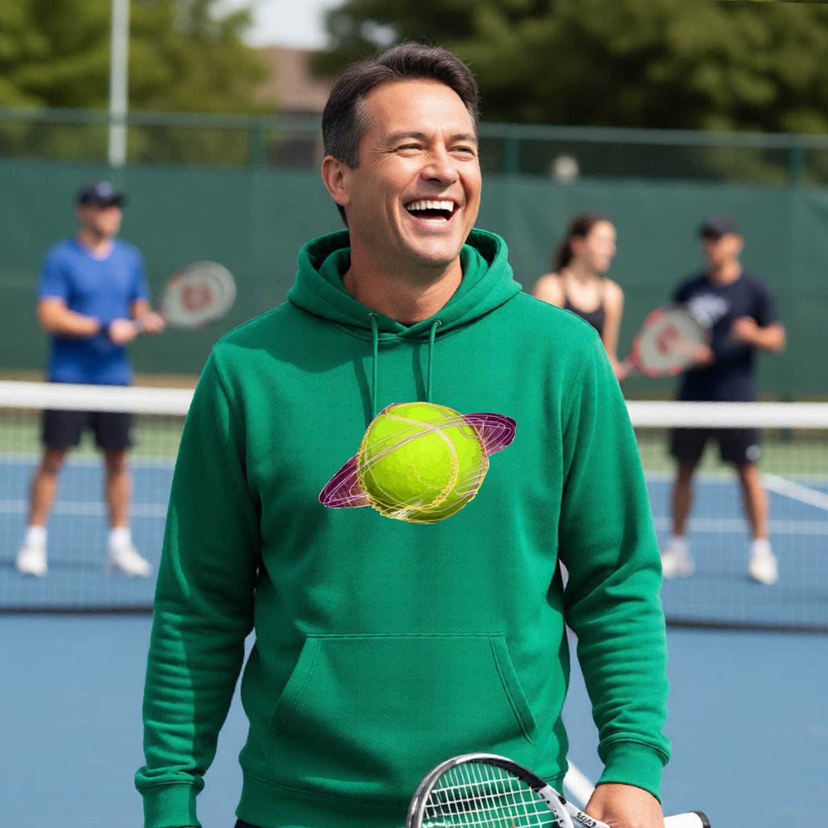A man on a tennis court wearing a green hoodie pullover with a graphic of a tennis ball in orbit, holding a tennis racket. Other players are visible in the background on the court.