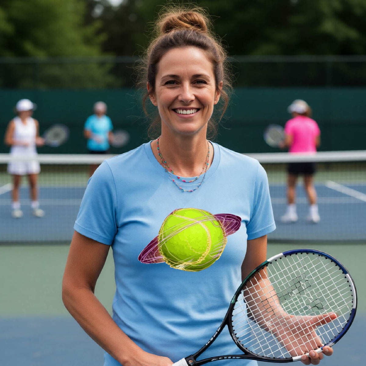 A woman on a tennis court wearing a blue short-sleeve t-shirt with a graphic of a tennis ball in orbit, holding a tennis racket. Other players are visible in the background on the court.