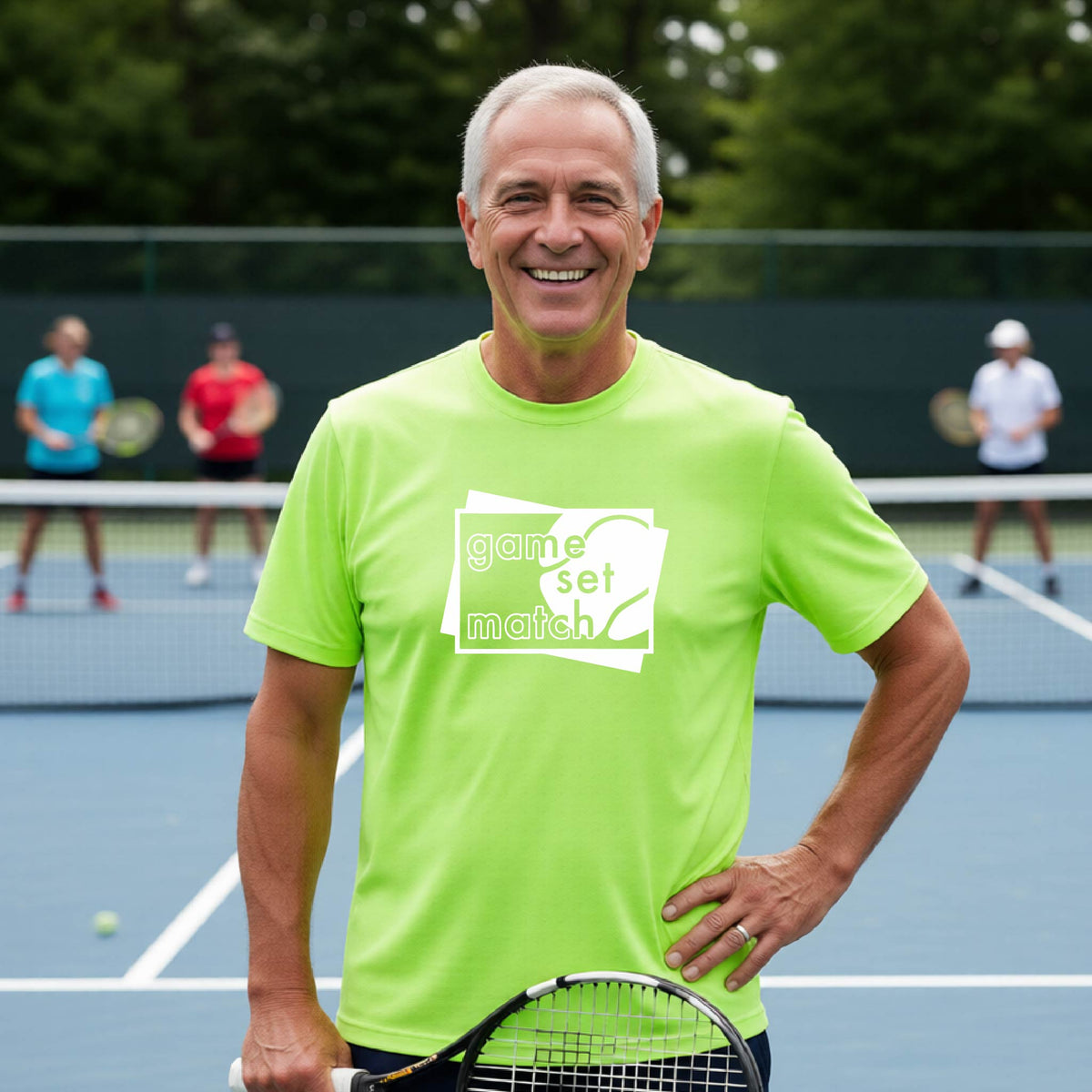 A man on a blue tennis court holds a tennis racket and wears a lime green short-sleeve T-shirt with a white graphic of two overlapping white and gray squares with the cut out words of ‘GAME SET MATCH” and a tennis ball, printed on the front of the shirt. 