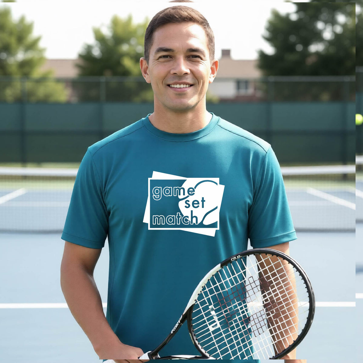 A man on a blue tennis court holds a tennis racket and wears a teal short-sleeve T-shirt with a white graphic of two overlapping white and gray squares with the cut out words of ‘GAME SET MATCH” and a tennis ball, printed on the front of the shirt. 