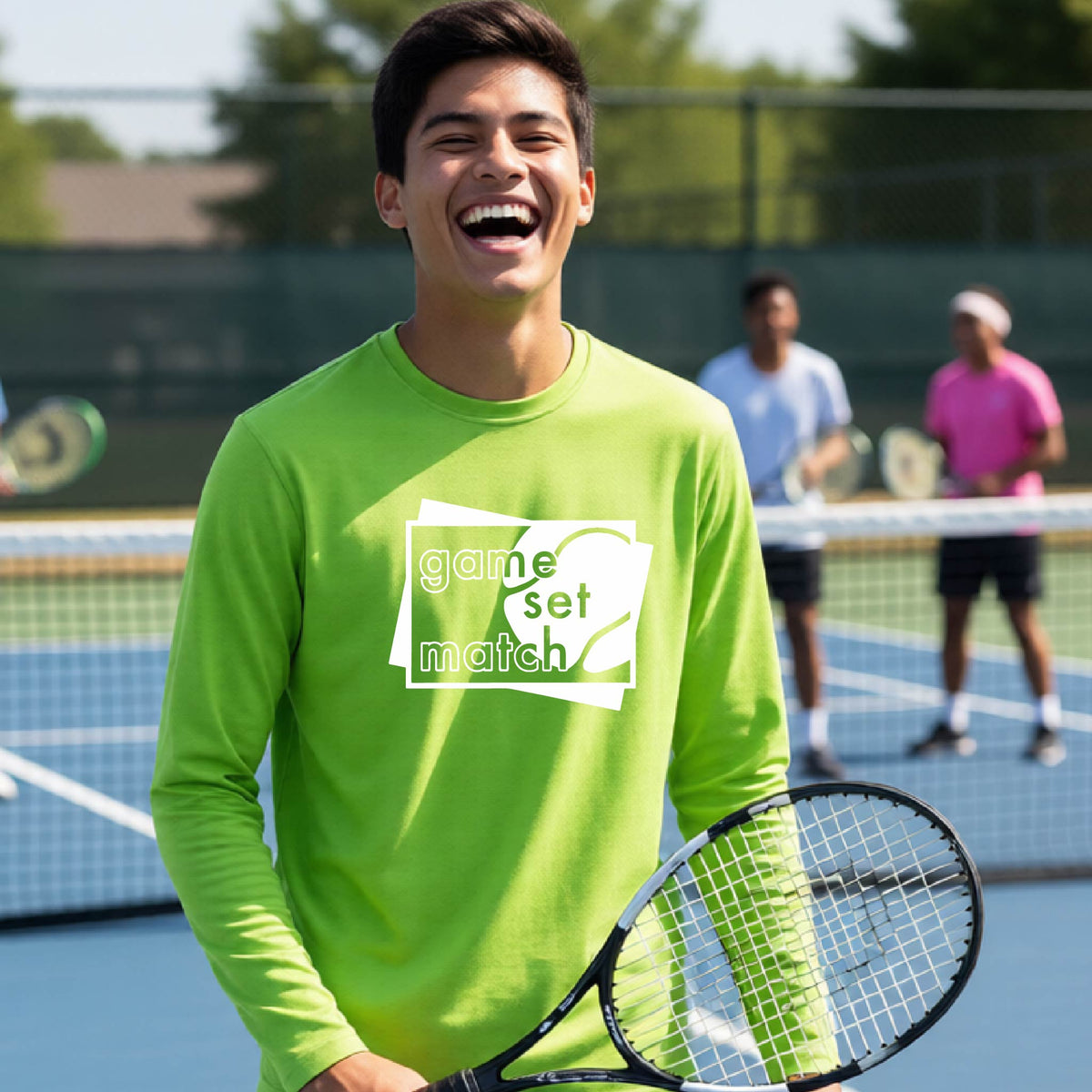 A young person on a blue tennis court holds a tennis racket and wears a lime green long-sleeve T-shirt with a white graphic of two overlapping white and gray squares with the cut out words of ‘GAME SET MATCH” and a tennis ball, printed on the front of the shirt. 