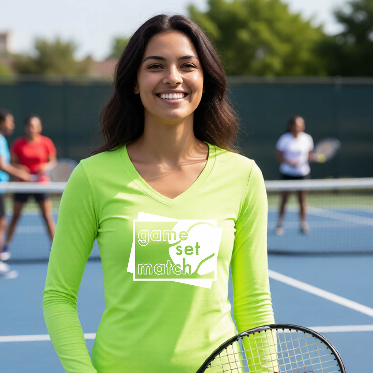 A woman on a blue tennis court holds a tennis racket and wears a lime green long-sleeve T-shirt with a white graphic of two overlapping white and gray squares with the cut out words of ‘GAME SET MATCH” and a tennis ball, printed on the front of the shirt. 