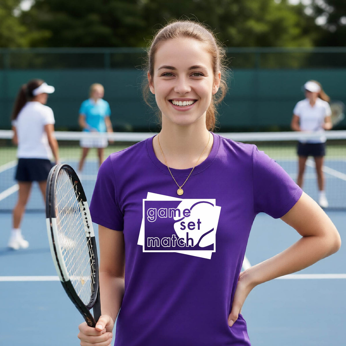 A wpman on a blue tennis court holds a tennis racket and wears a purple short-sleeve T-shirt with a white graphic of two overlapping white and gray squares with the cut out words of ‘GAME SET MATCH” and a tennis ball, printed on the front of the shirt. 