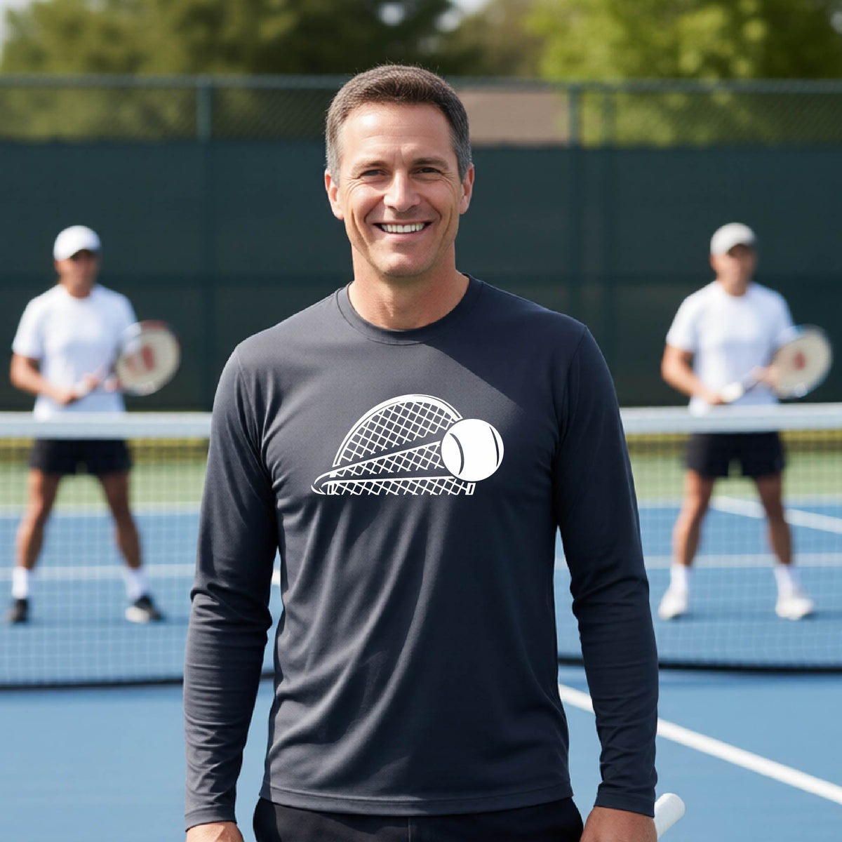 A man on a blue tennis court holds a tennis racket and wears a dark gray long-sleeve T-shirt with a white graphic of a half a tennis racquet with a ball streaking over it. 