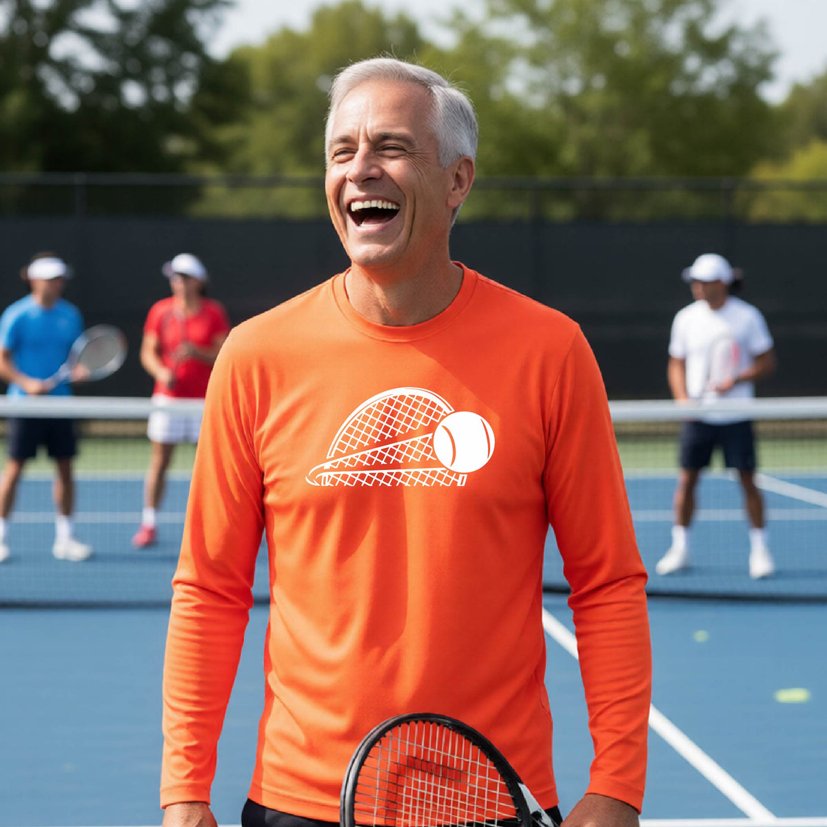 A man on a blue tennis court holds a tennis racket and wears an orange long-sleeve T-shirt with a white graphic of a half a tennis racquet with a ball streaking over it. 