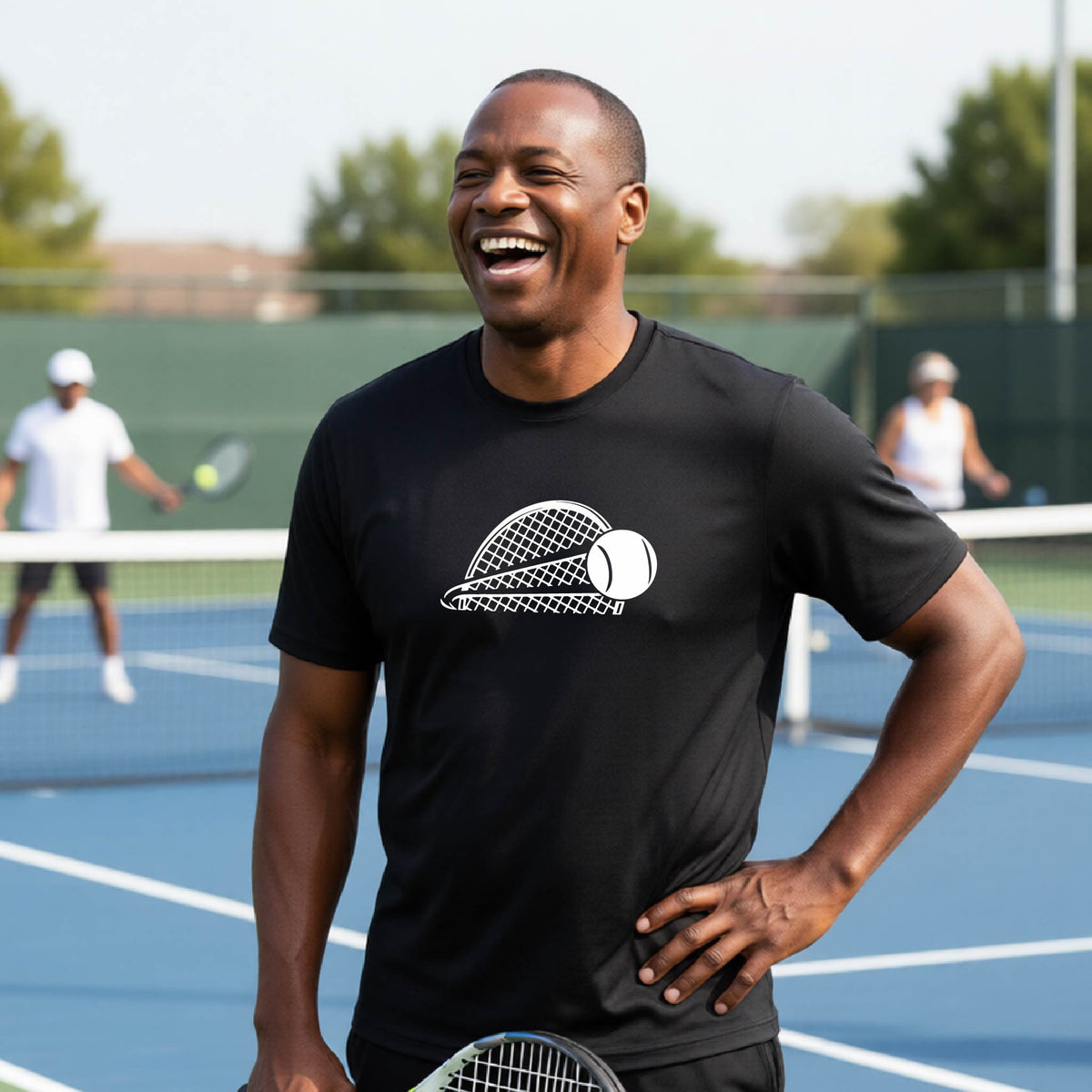 A man on a blue tennis court holds a tennis racket and wears a black short-sleeve T-shirt with a white graphic of a half a tennis racquet with a ball streaking over it. 