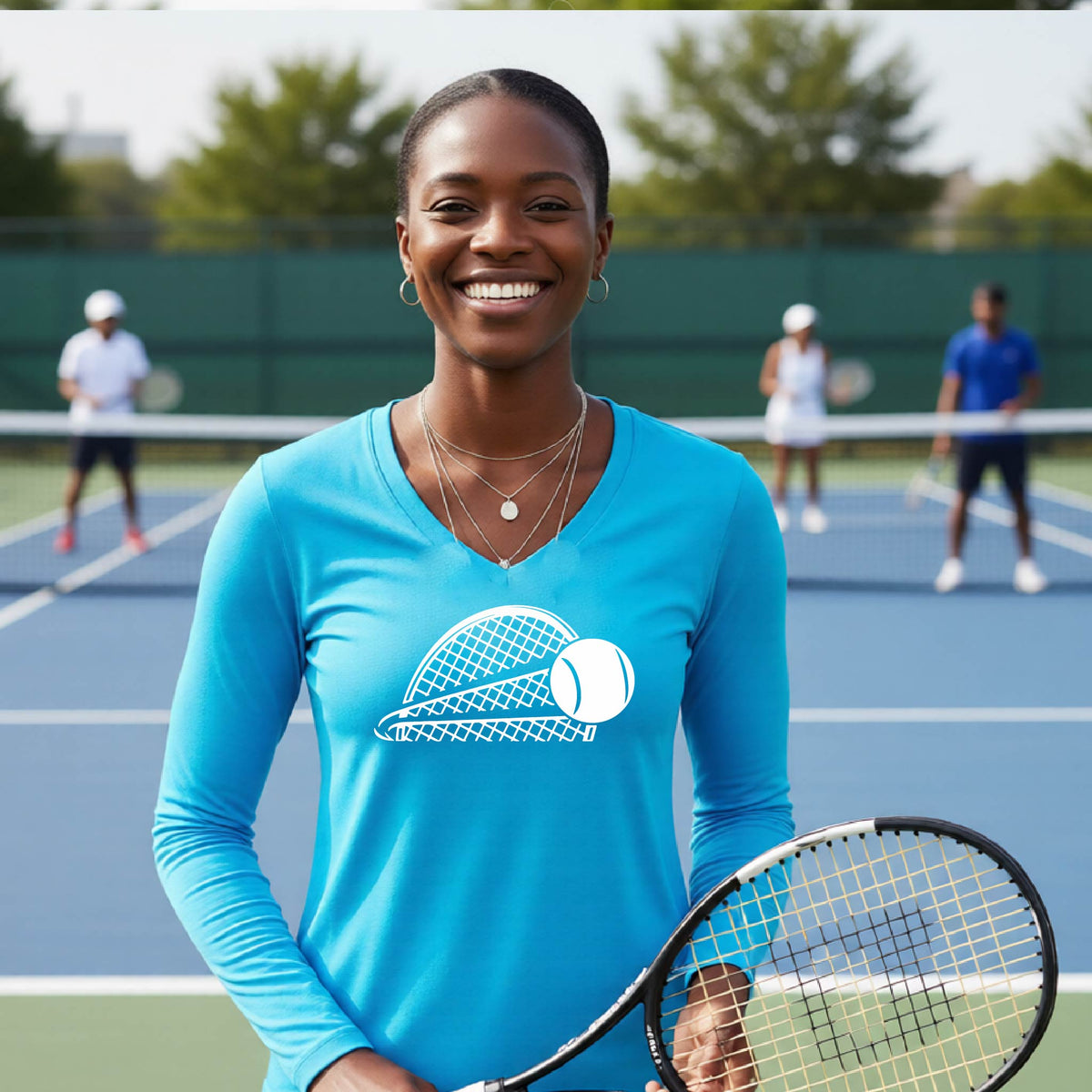 A woman on a blue tennis court holds a tennis racket and wears a bright blue long-sleeve T-shirt with a white graphic of a half a tennis racquet with a ball streaking over it. 