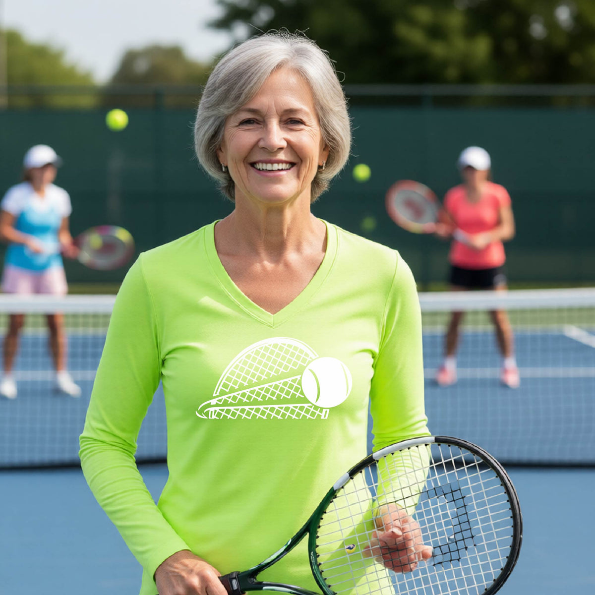 A woman on a blue tennis court holds a tennis racket and wears a lime green long-sleeve T-shirt with a white graphic of a half a tennis racquet with a ball streaking over it. 