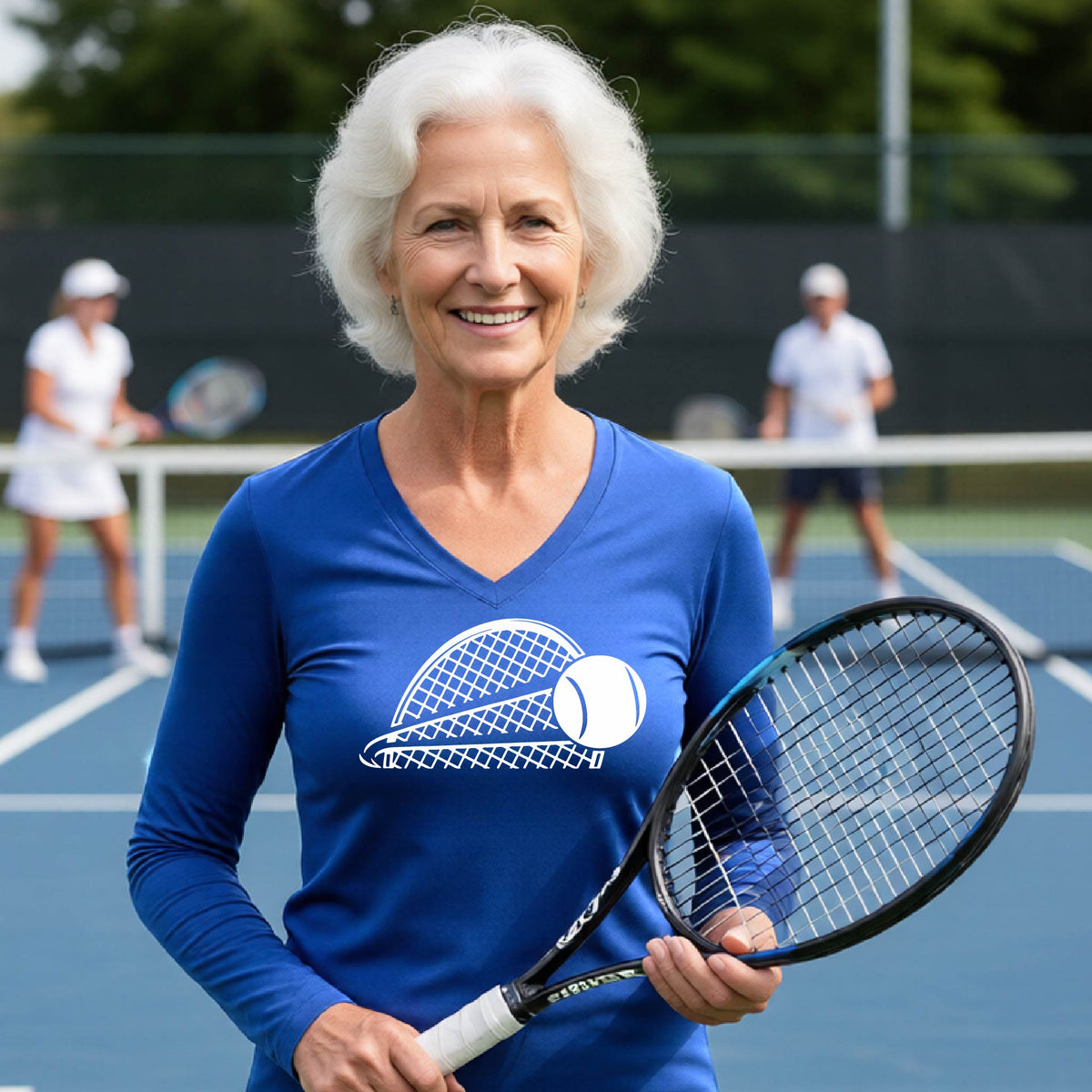 A woman on a blue tennis court holds a tennis racket and wears a royal blue long-sleeve T-shirt with a white graphic of a half a tennis racquet with a ball streaking over it. 