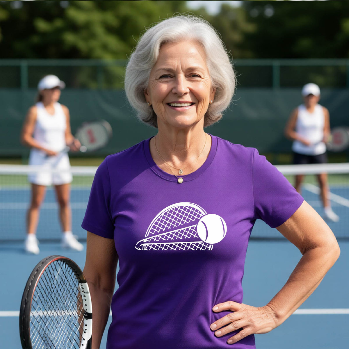 A woman on a blue tennis court holds a tennis racket and wears a purple short-sleeve T-shirt with a white graphic of a half a tennis racquet with a ball streaking over it. 