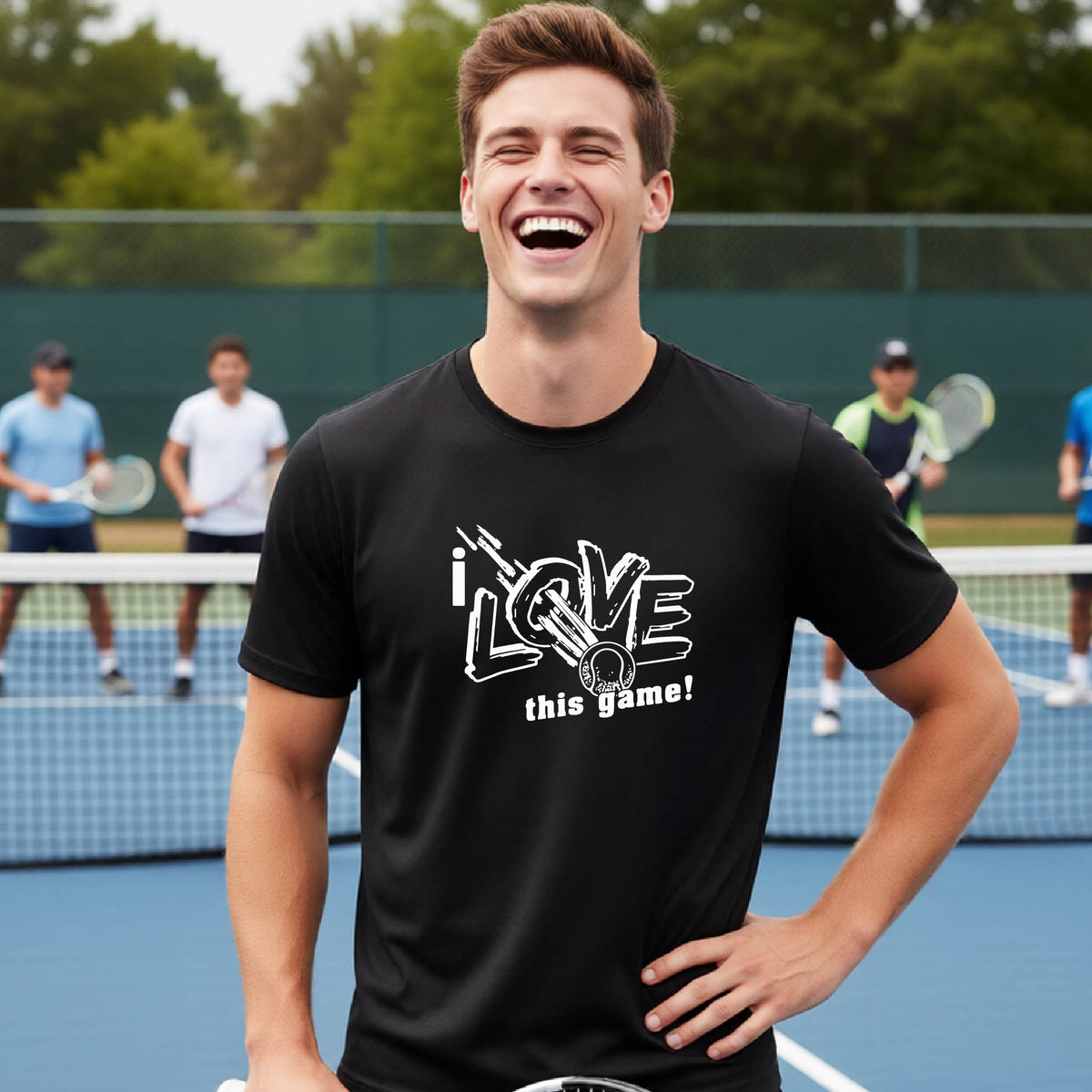 A man laughing on a tennis court wearing a black t-shirt with a white graphic that reads 'i LOVE this game!' and a white tennis ball.