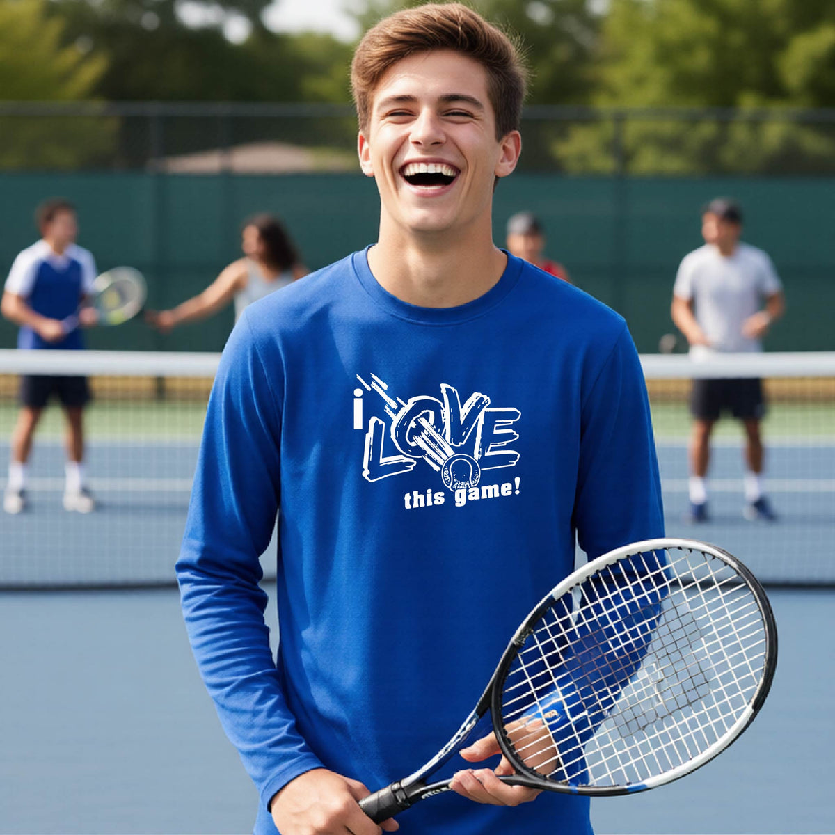 A young man laughing on a tennis court wearing a royal blue long-sleeve t-shirt with a white graphic that reads 'I LOVE this game!'. He is holding a tennis racket, with other players and the court visible in the background.