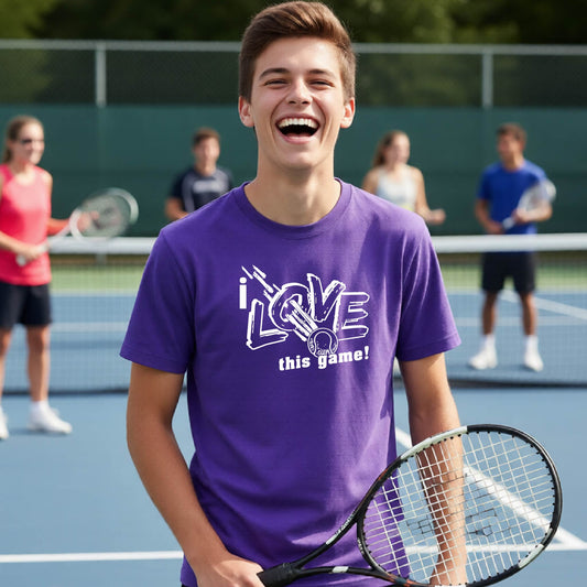A young man laughing on a tennis court wearing a purple t-shirt with a white graphic that reads 'i LOVE this game!'.