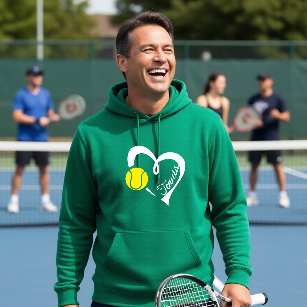 A man on a tennis court wearing a bright green hoodie with a white heart graphic, a yellow tennis ball, and the name 'Tennis' printed on the front. In the background, other tennis players are visible on the court.