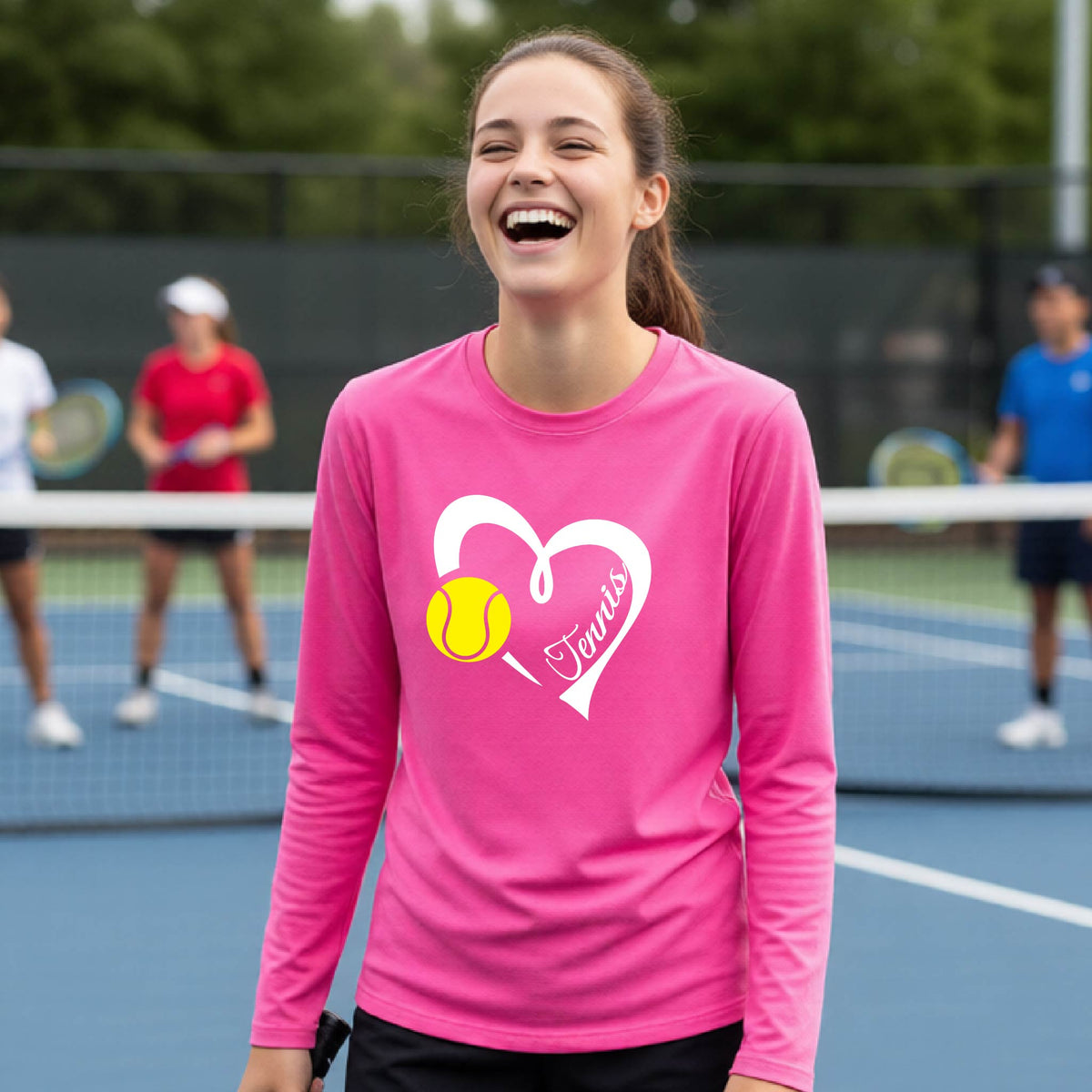A woman laughing on a tennis court wearing a bright pink long-sleeve shirt with a white heart, yellow tennis ball graphic, and the word 'Tennis' printed on the front.