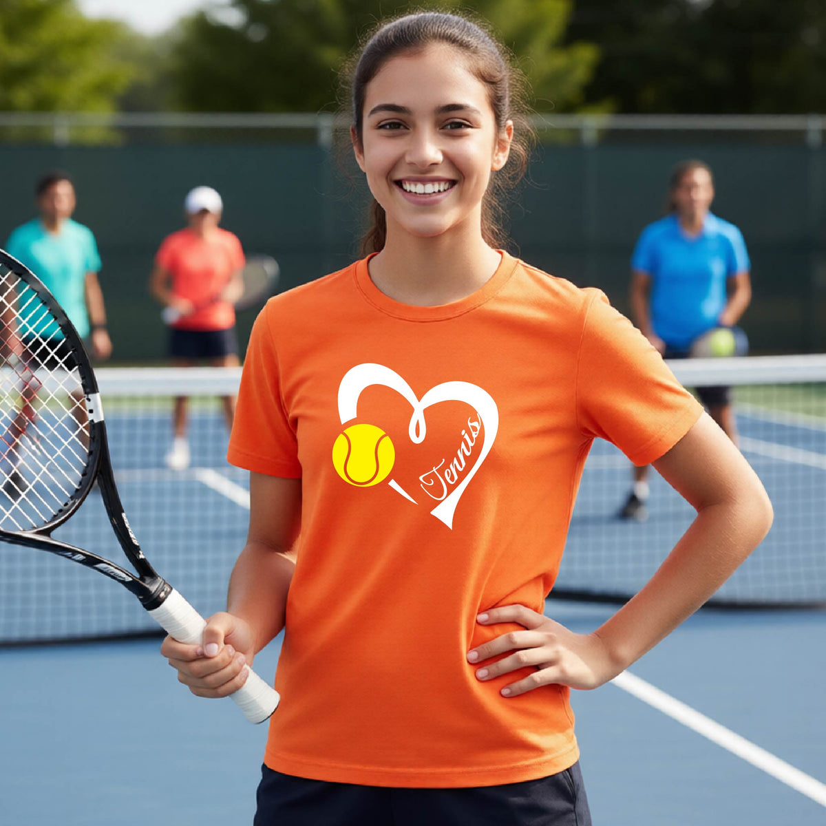 A smiling young woman on a tennis court wearing an orange T-shirt with a white heart graphic, a yellow tennis ball, and the name 'Tennis' printed on the front. She holds a tennis racket, with other players blurred in the background.