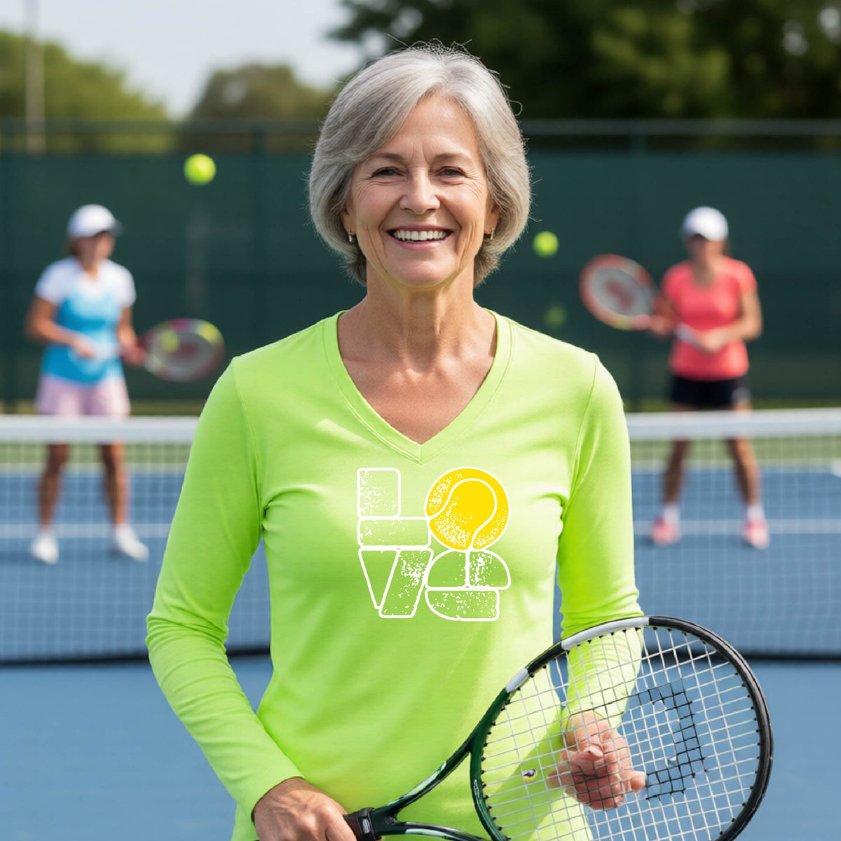 A woman wearing a lime long-sleeve t-shirt with a white and yellow tennis-themed graphic "LOVE" with a tennis ball replacing the O, with a tennis  court and players in the background.