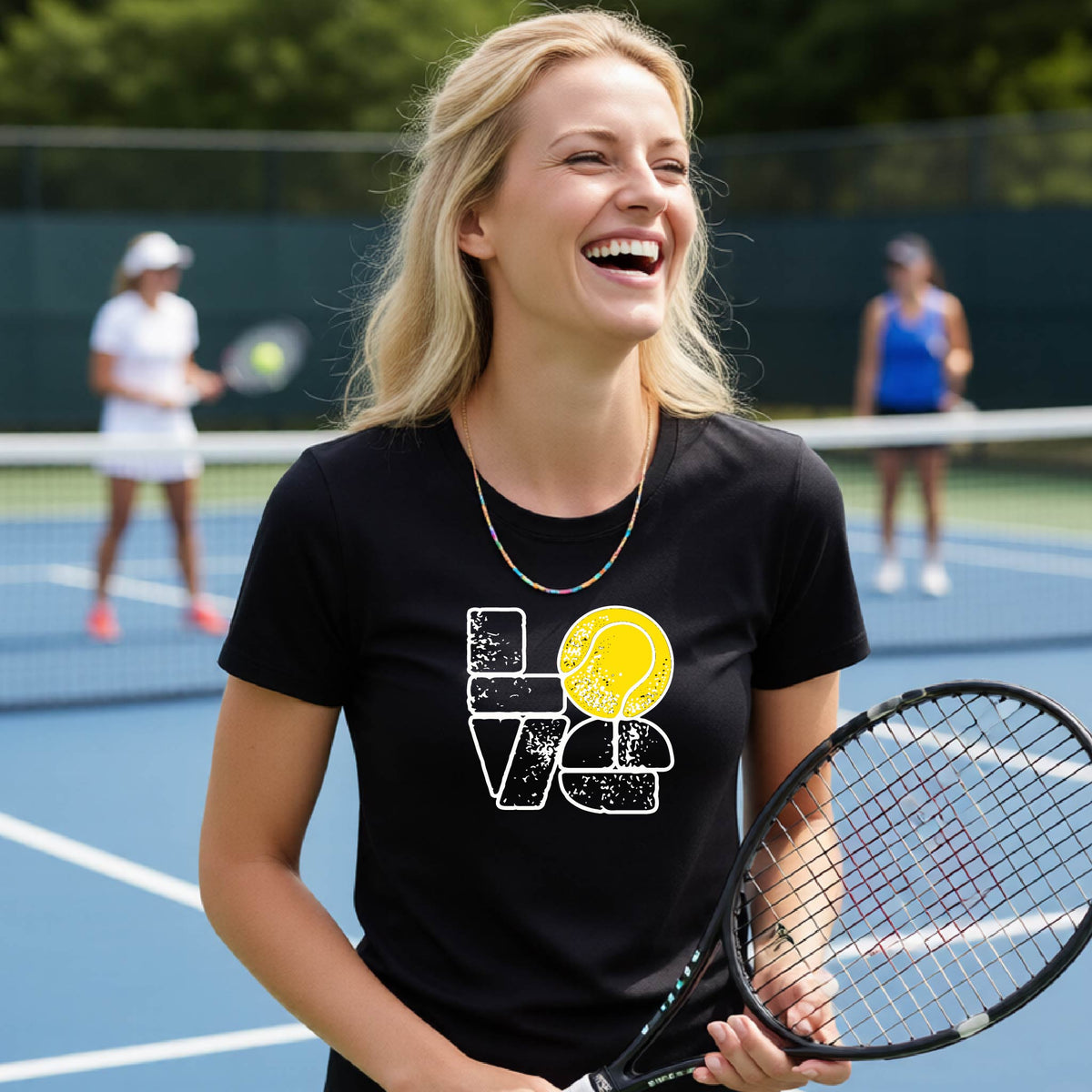 A woman wearing a black short-sleeve t-shirt with a white and yellow tennis-themed graphic "LOVE" with a tennis ball replacing the O, with a tennis  court and players in the background.