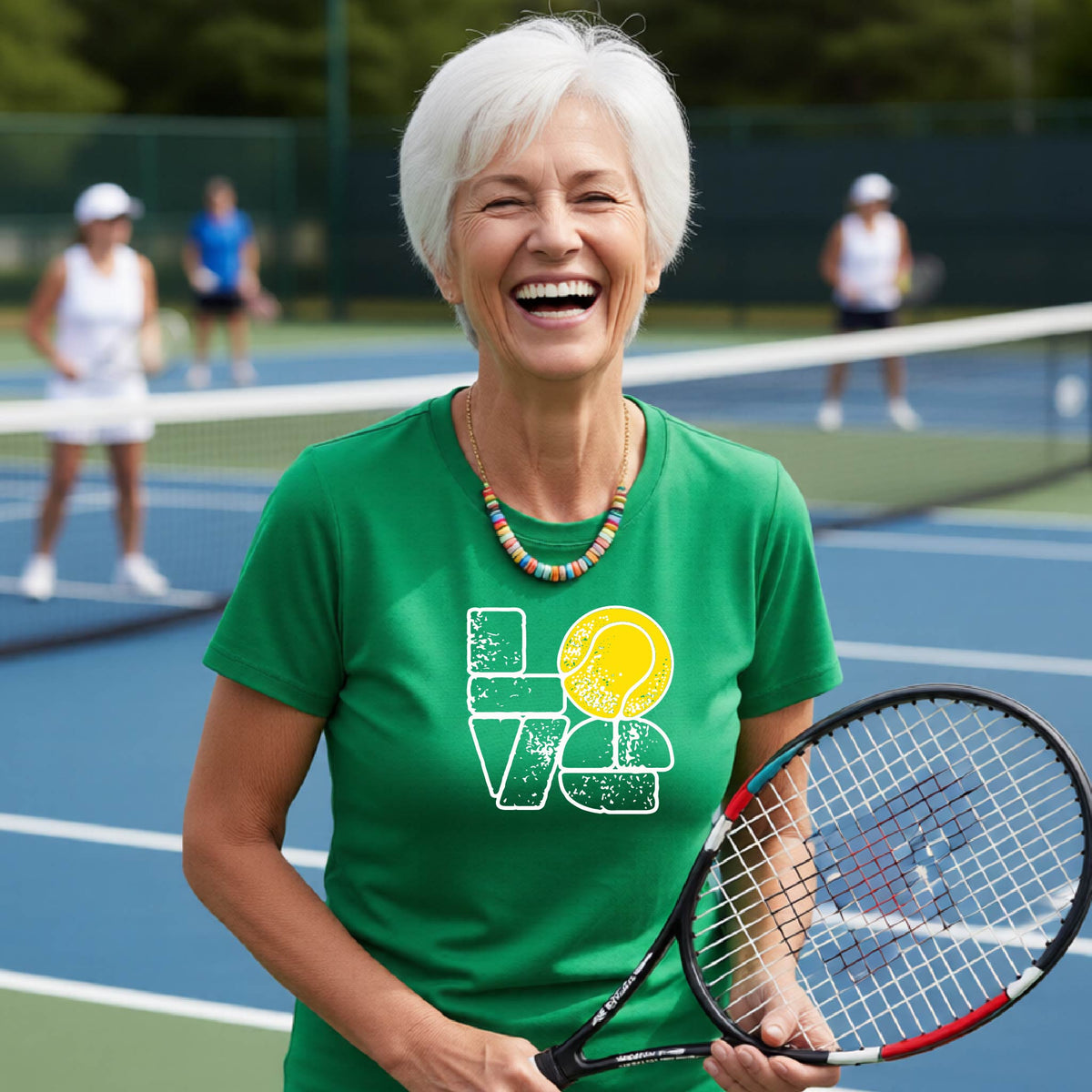 A woman wearing a green short-sleeve t-shirt with a white and yellow tennis-themed graphic "LOVE" with a tennis ball replacing the O, with a tennis  court and players in the background.