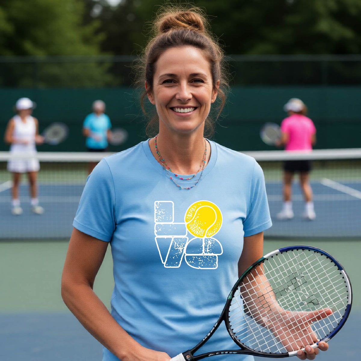 A woman wearing a blue short-sleeve t-shirt with a white and yellow tennis-themed graphic "LOVE" with a tennis ball replacing the O, with a tennis  court and players in the background.